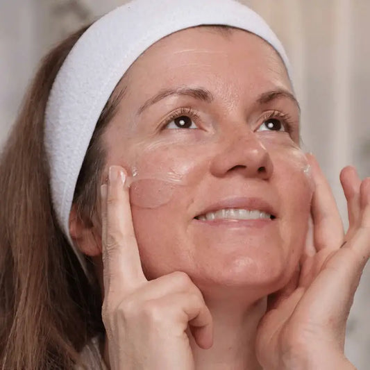 Femme avec un bandeau blanc appliquant le baume nettoyant seul geste pour peaux sèches