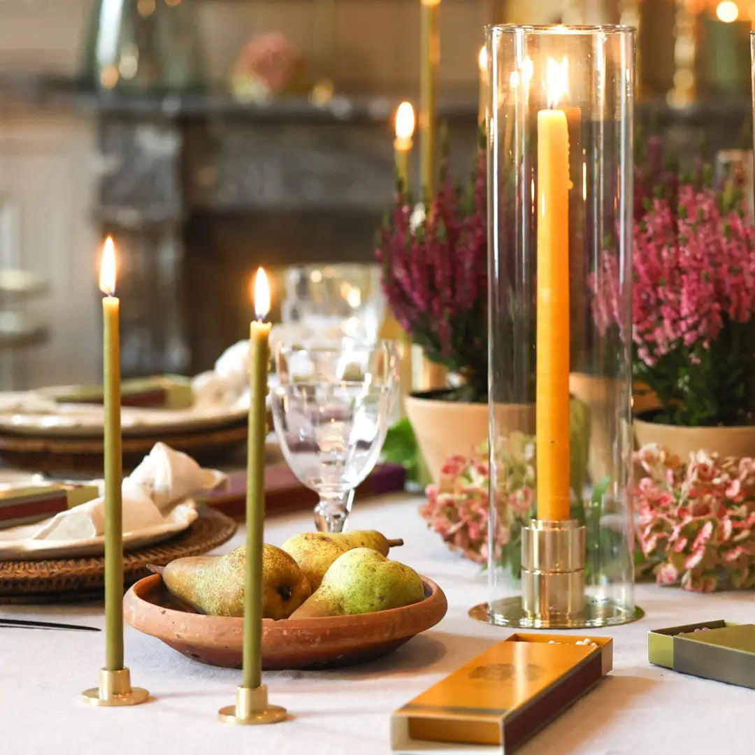 Table dressée avec bougies fines en porte-cierges laiton, lumière douce, bol de poires