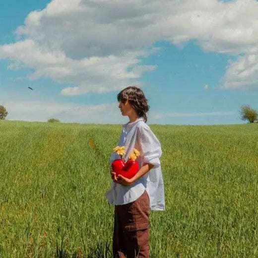 Femme dans un champ avec un vase coeur rouge rempli de fleurs jaunes