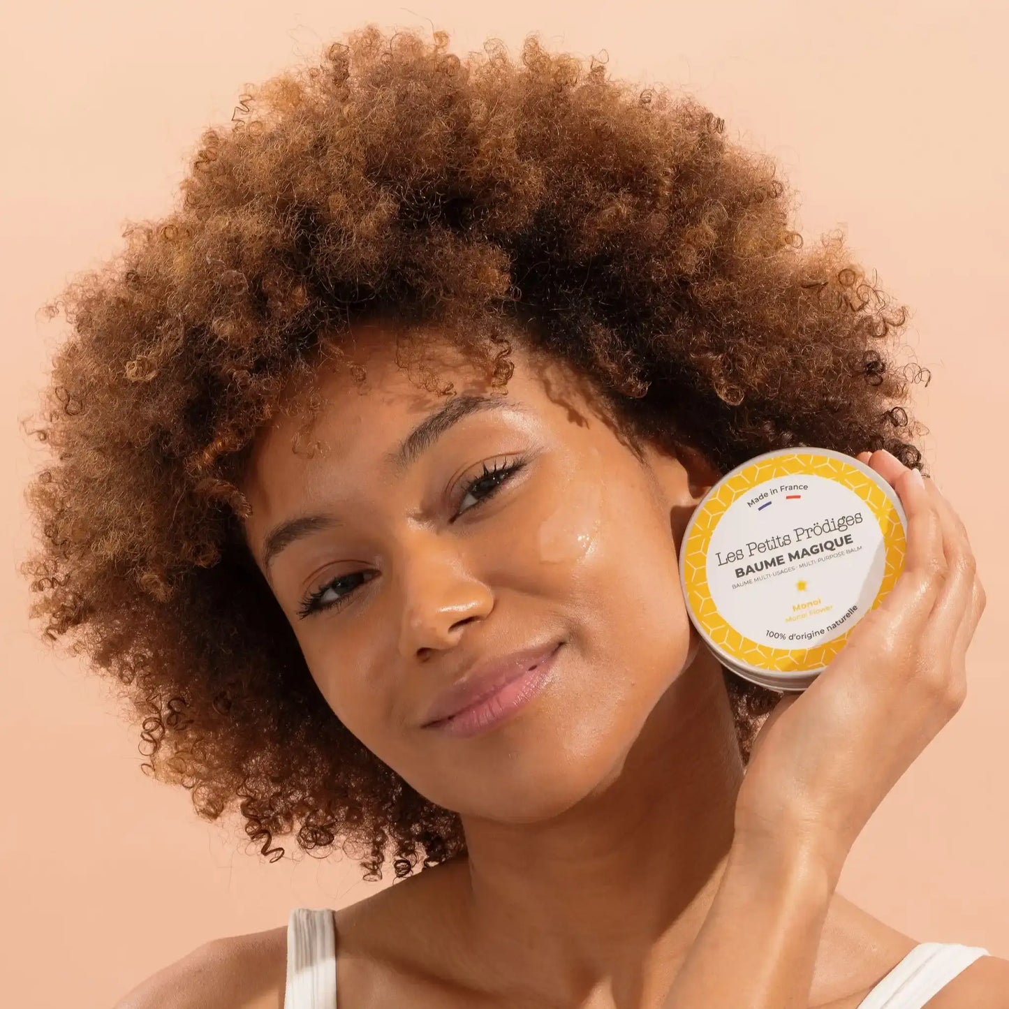Femme aux cheveux bouclés applique Baume Multi Usage au Monoi sur son visage pour routine beauté peaux sensibles