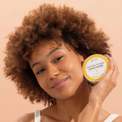 Femme aux cheveux bouclés applique Baume Multi Usage au Monoi sur son visage pour routine beauté peaux sensibles