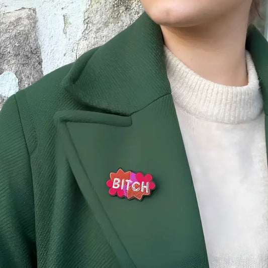 Personne portant une veste verte foncée avec une broche bitch brodée et fils brillants