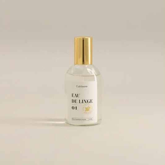 Bouteille en verre clair avec un bouchon en or contenant un liquide clair pour Brume de linge 100 ml