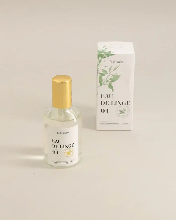 Brume de linge 100 ml en bouteille spray verre clair avec capuchon or et boîte carton blanc, motifs feuilles vertes, Eau de Linge 01 pour redonner vie et fraîcheur naturelle