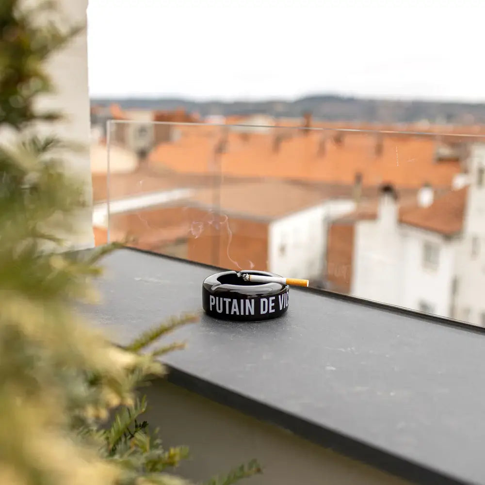 Cendrier Putain De Vie noir avec message audacieux et cigarette allumée
