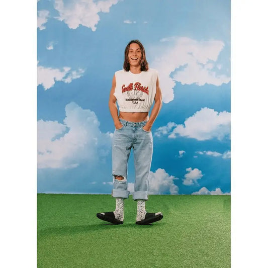 Personne en crop top blanc, jeans déchirés, chaussettes fantaisie Fromage Bleu à touche d’humour et sandales slides noires