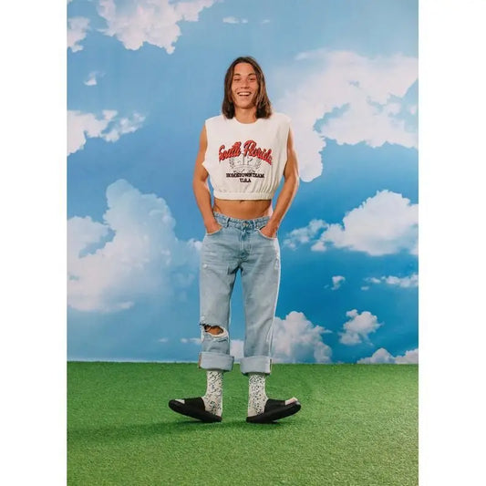 Personne en crop top blanc sans manches, jeans bleu déchiré, chaussettes fromage bleu, slides noirs pour confort optimal