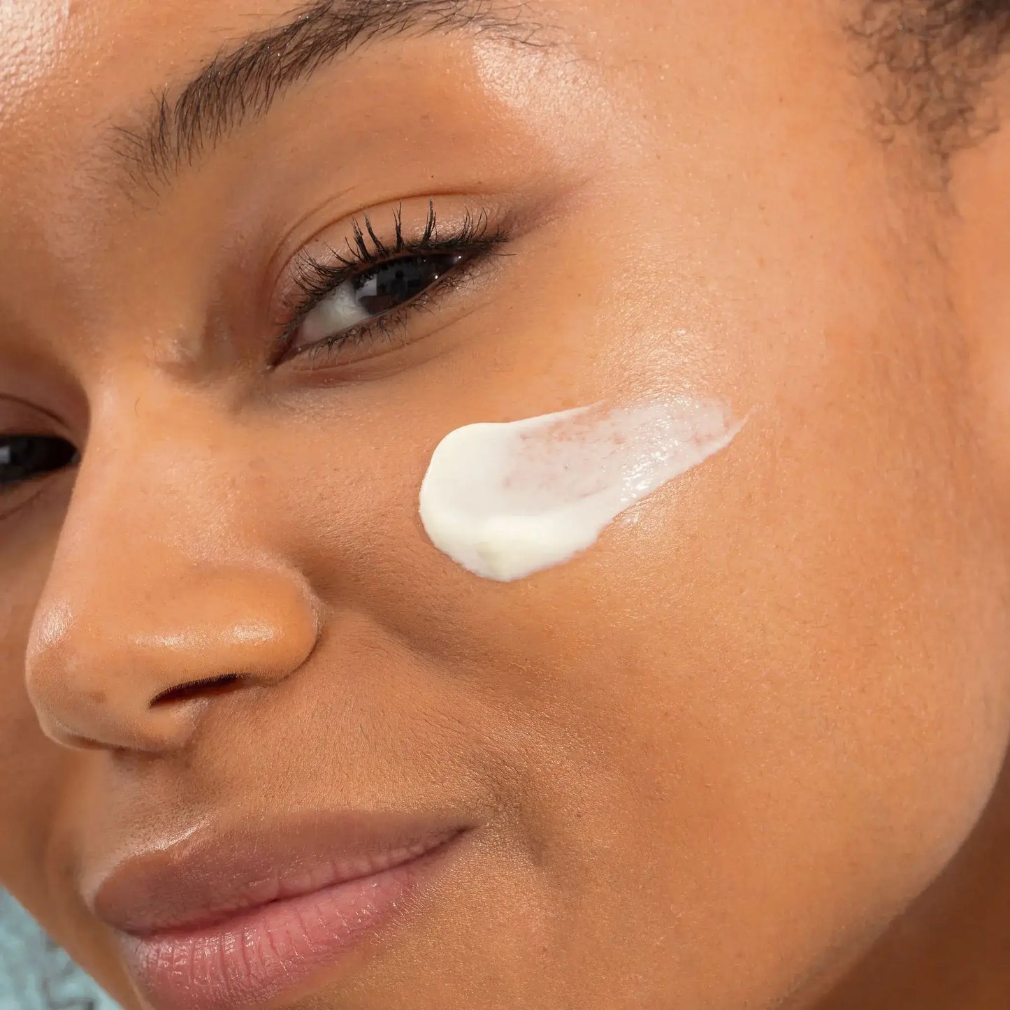 Femme avec crème solaire SPF50+ texture légère sur la joue