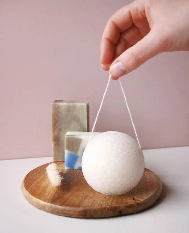Éponge konjac blanche et duveteuse suspendue par un fil pour routine beauté zéro déchet