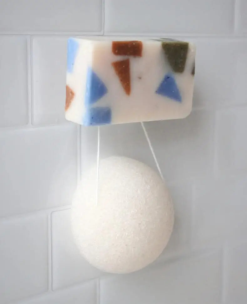 Éponge konjac blanche rectangulaire avec incrustations bleues et brunes sur mur carrelé
