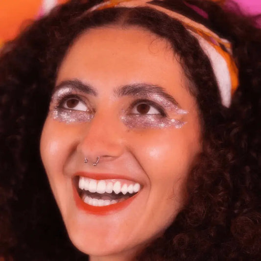 Femme souriante avec maquillage pailleté et piercing nasal, baume pailleté éclat naturel