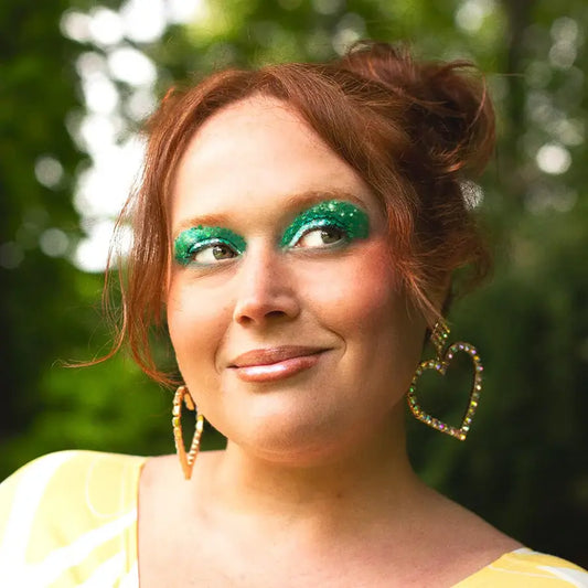 Femme rousse aux yeux verts pailletés et boucles d’oreilles cœur, gel pailleté Polysirène