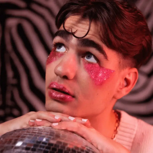 Personne au maquillage audacieux avec gel pailleté rose sous les yeux, menton sur boule disco