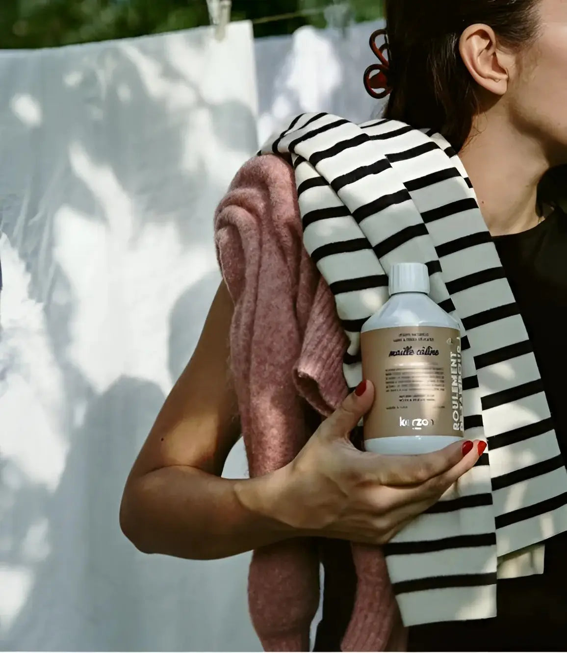 Bouteille blanche de lessive liquide maille câline pour cycles délicats, tenue par une personne