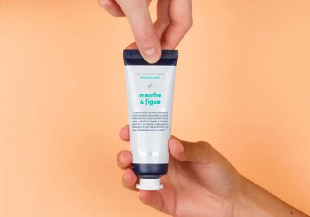 Tube blanc de lotion mains menthe figue 50ml, tenu dans les mains sur fond orange