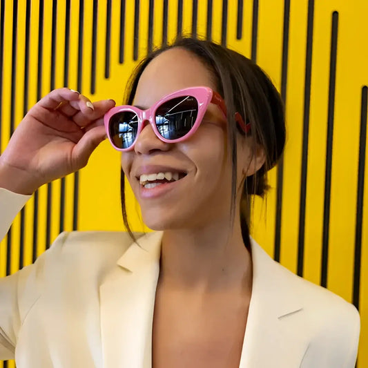 Femme souriante en blazer crème et lunettes soleil better late than ugly pour protection visuelle