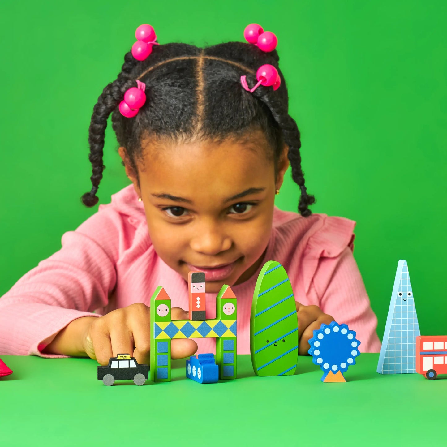 Enfant aux tresses et pinces roses joue avec Mini Ville Bois Kidoki Londres, jouets durables en bois