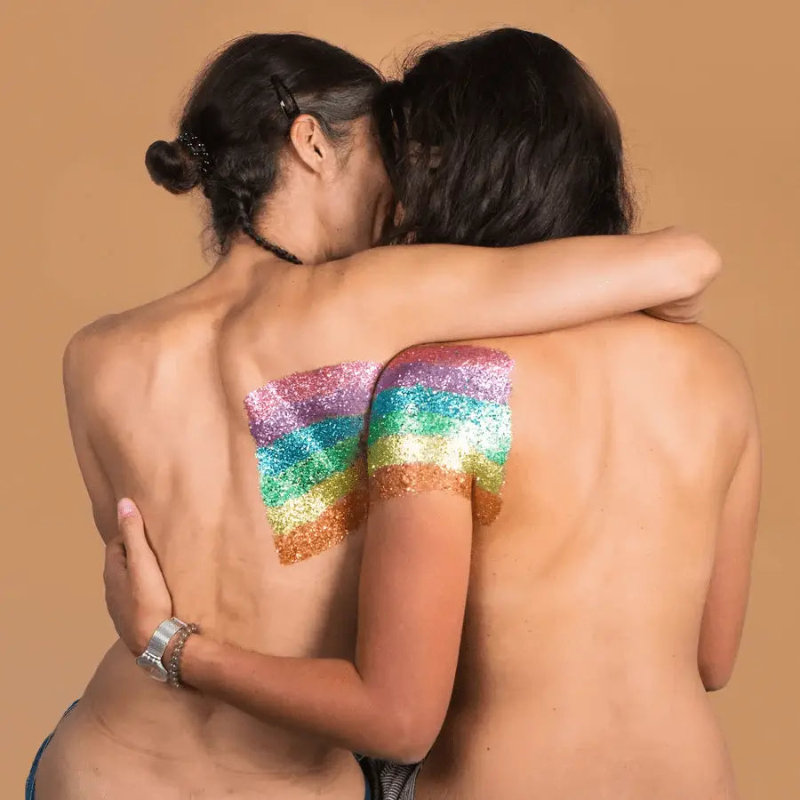 Deux femmes enlacées dos nu, paillettes arc-en-ciel sur épaule