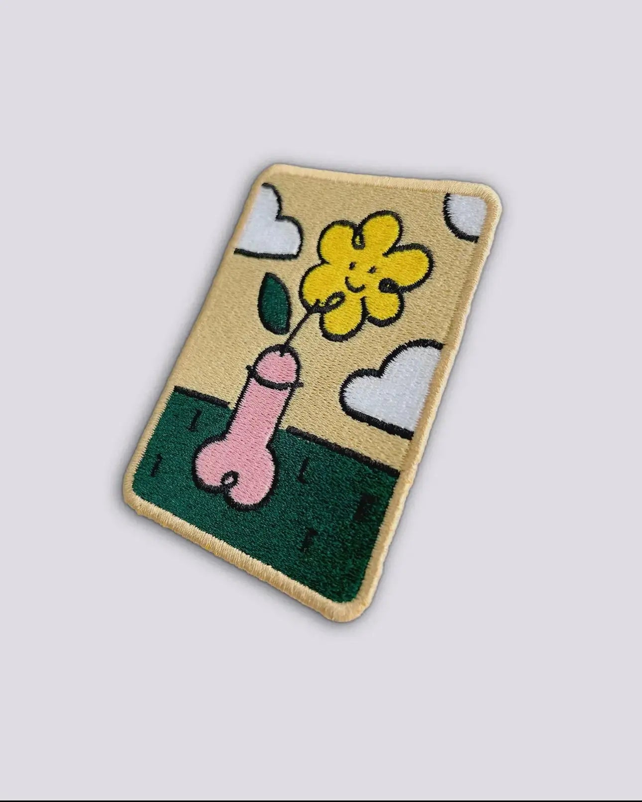 Tapis Patch Whoopsy Daisy avec phallus rose en pot fleuri jaune souriant sur herbe verte