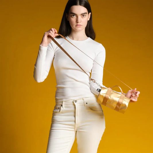 Femme en chemise blanche et jeans blancs tenant sac week-end gold chic