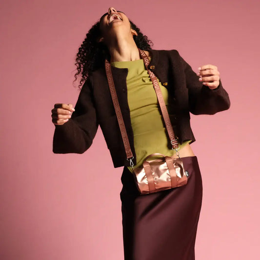 Femme en veste marron, top vert, jupe noire et mini sac weekender rose doré métallique