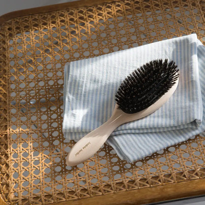 Petite brosse à cheveux en bois aux poils noirs sur serviette rayée bleu clair et blanc pour soin capillaire