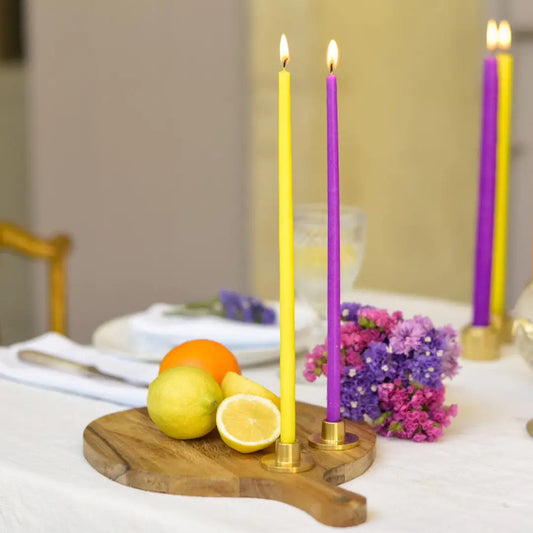 Deux bougies fines jaune et violet allumées en porte-cierges en laiton