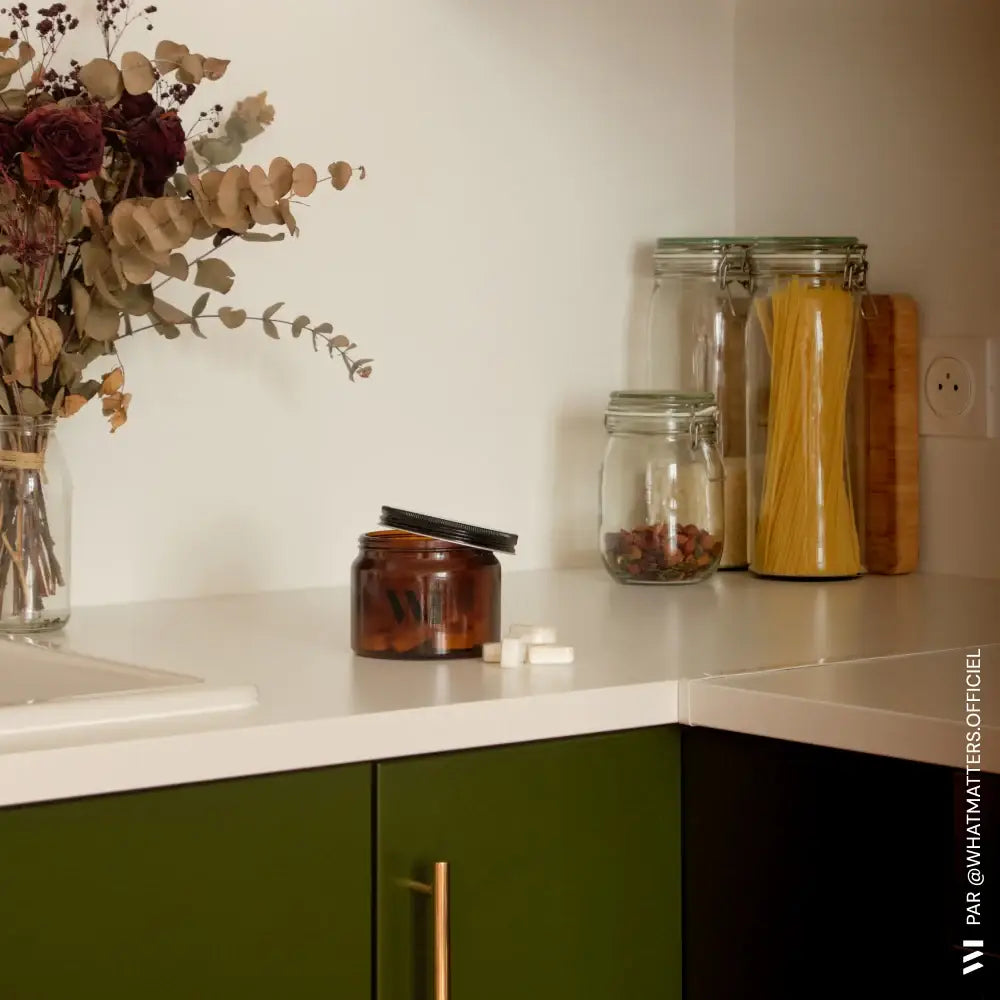 Pot lave-vaisselle X20 240g en pot en verre ambré foncé à couvercle noir ouvert sur comptoir blanc