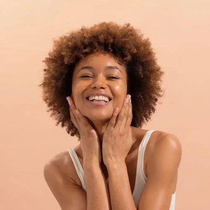 Femme souriante avec cheveux bouclés touchant son visage, nettoyant visage certifié bio