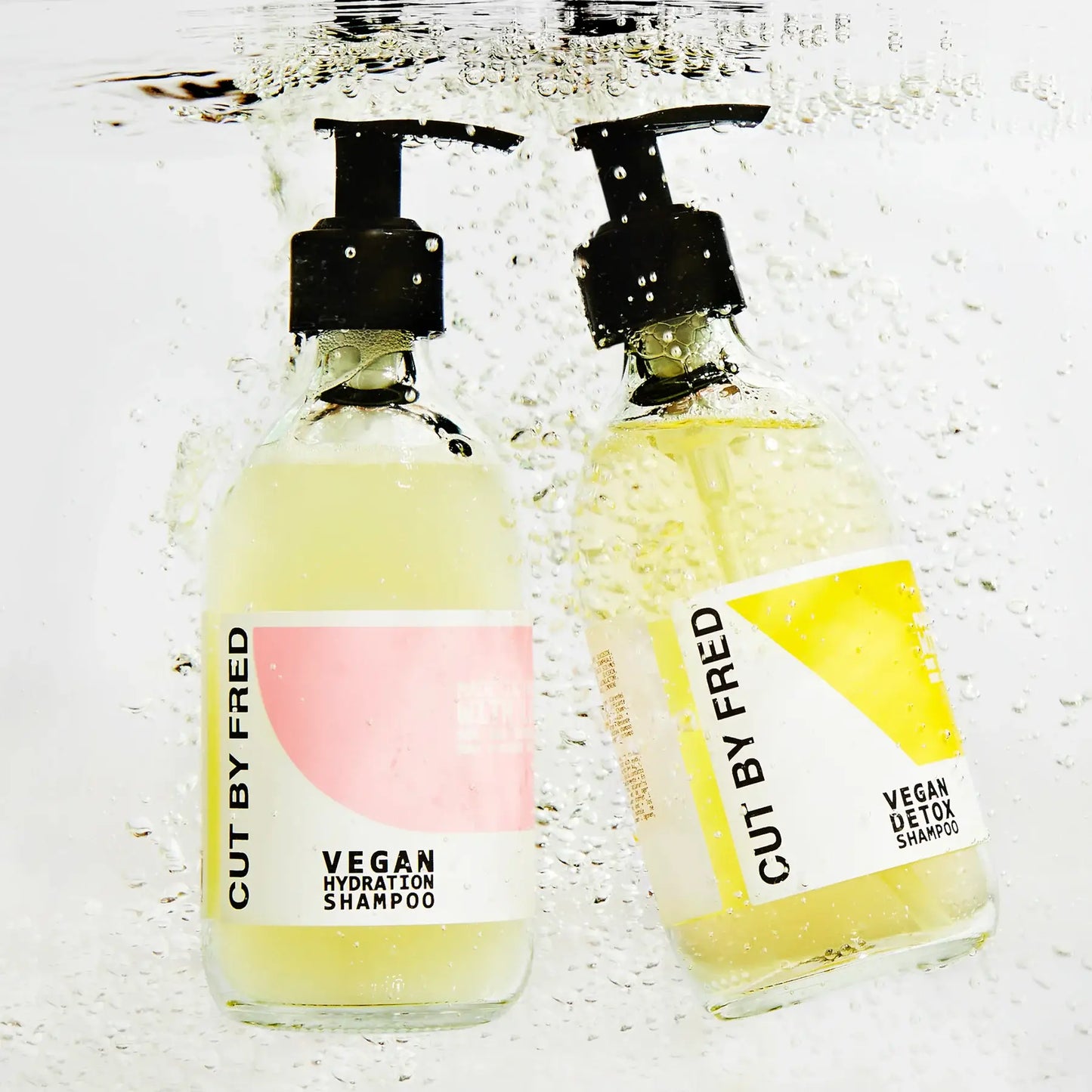 Deux bouteilles rechargeables de shampoing liquide hydratant vegan pour cheveux secs, immergées dans l’eau
