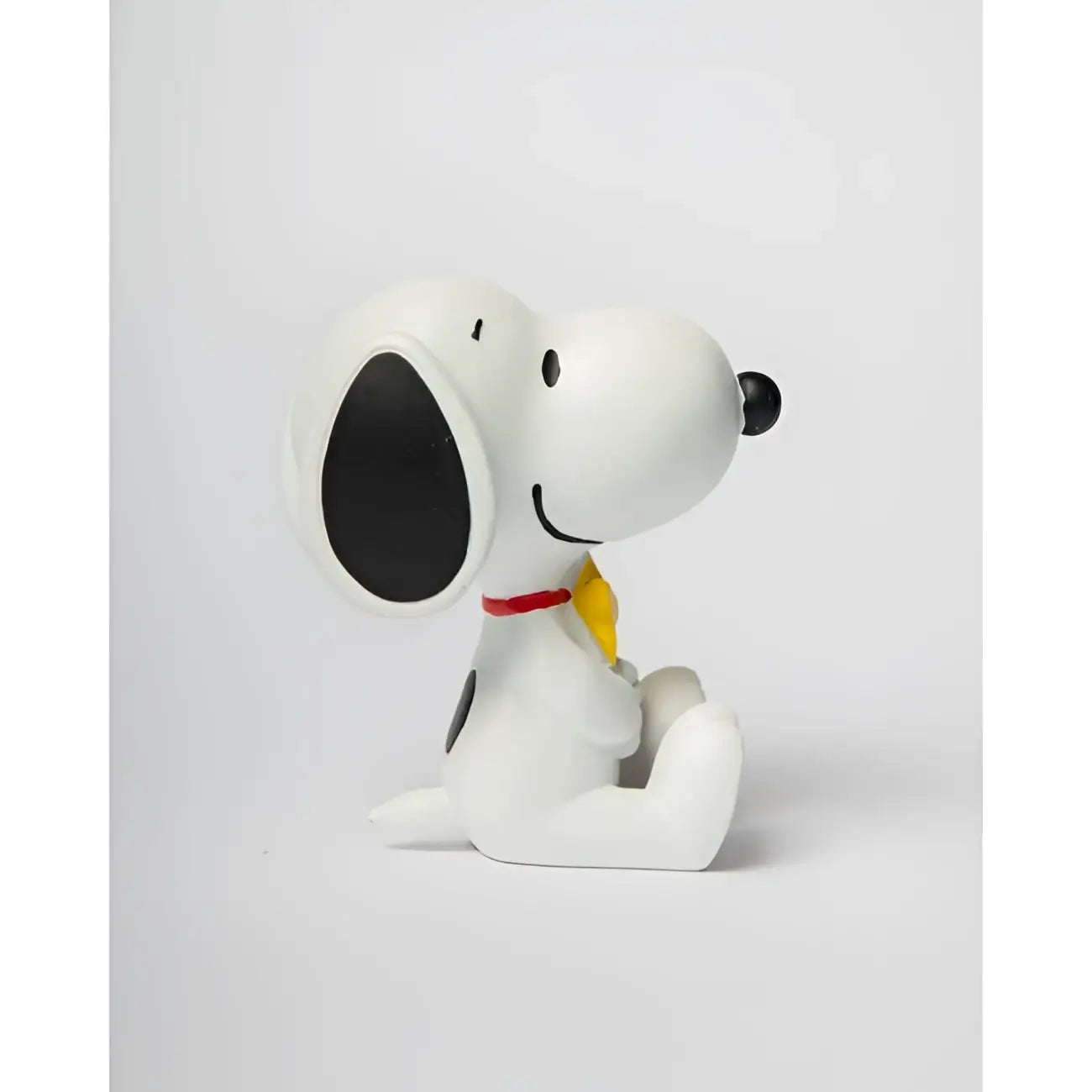 Statue Snoopy blanche avec oreilles noires, collier rouge et nœud papillon jaune, touche d’humour