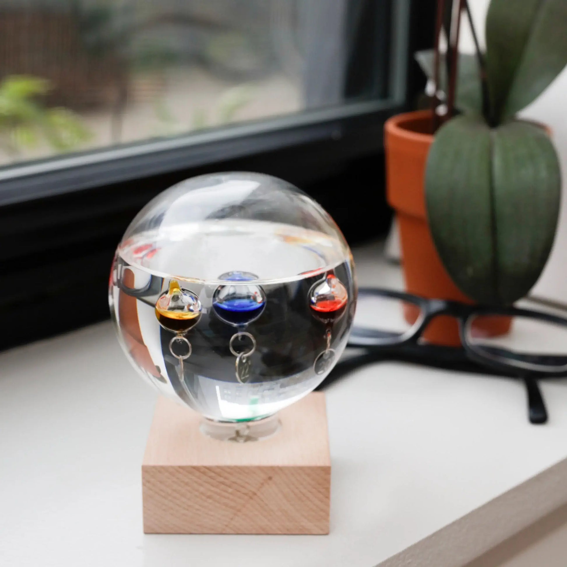 Thermomètre Galilée en verre clair avec sphères liquides colorées et anneaux argentés, matériaux nobles invitant à ralentir