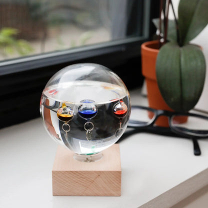 Thermomètre Galilée en verre clair avec sphères liquides colorées et anneaux argentés, matériaux nobles invitant à ralentir