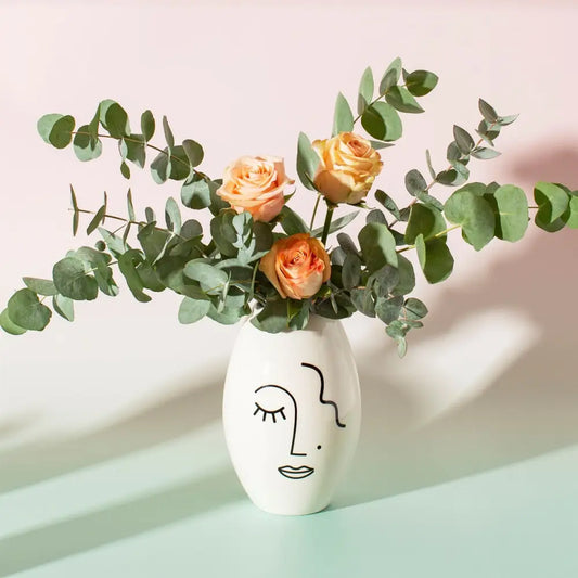 Vase visage abstrait blanc avec visage minimaliste, orange roses et eucalyptus