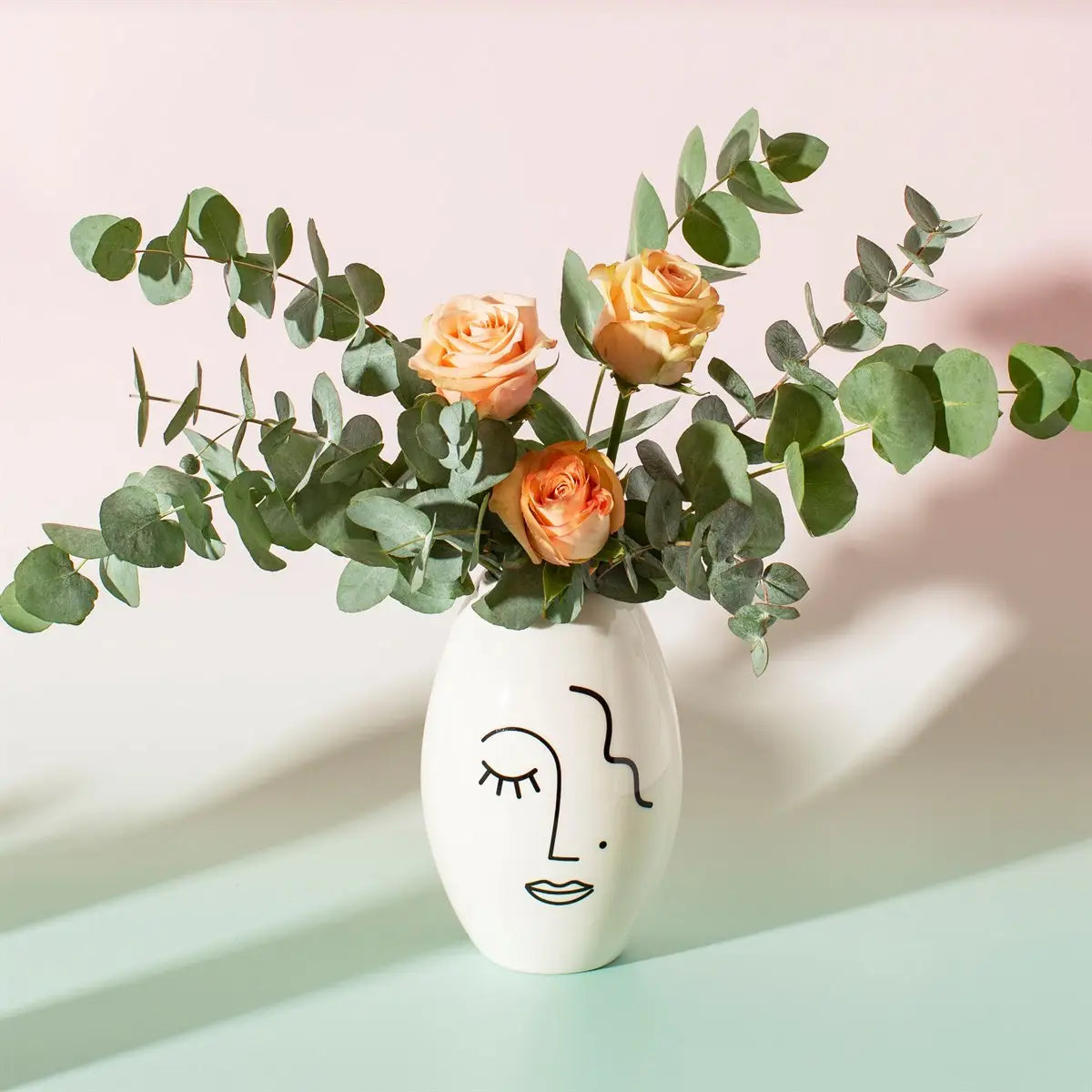 Vase Visage Abstrait blanc avec roses orange et eucalyptus, décoration florale